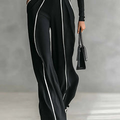 Black wide-leg pants and high-neck long-sleeve top with white piping and waist belt buckle.
