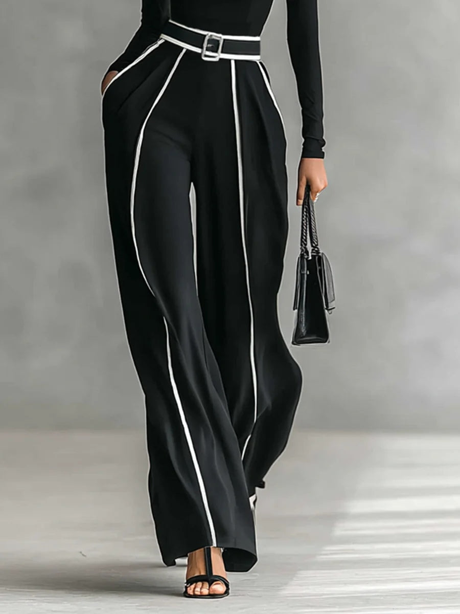 Black wide-leg pants and high-neck long-sleeve top with white piping and waist belt buckle.