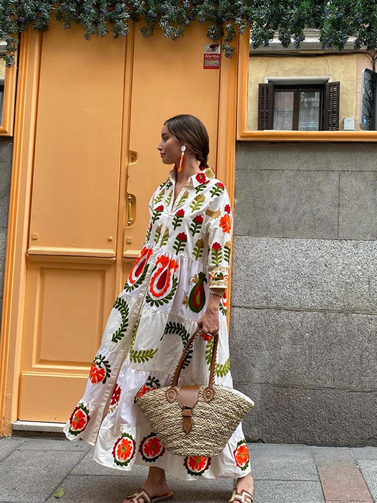 White long-sleeve tiered dress with bold red, green, and orange floral embroidery