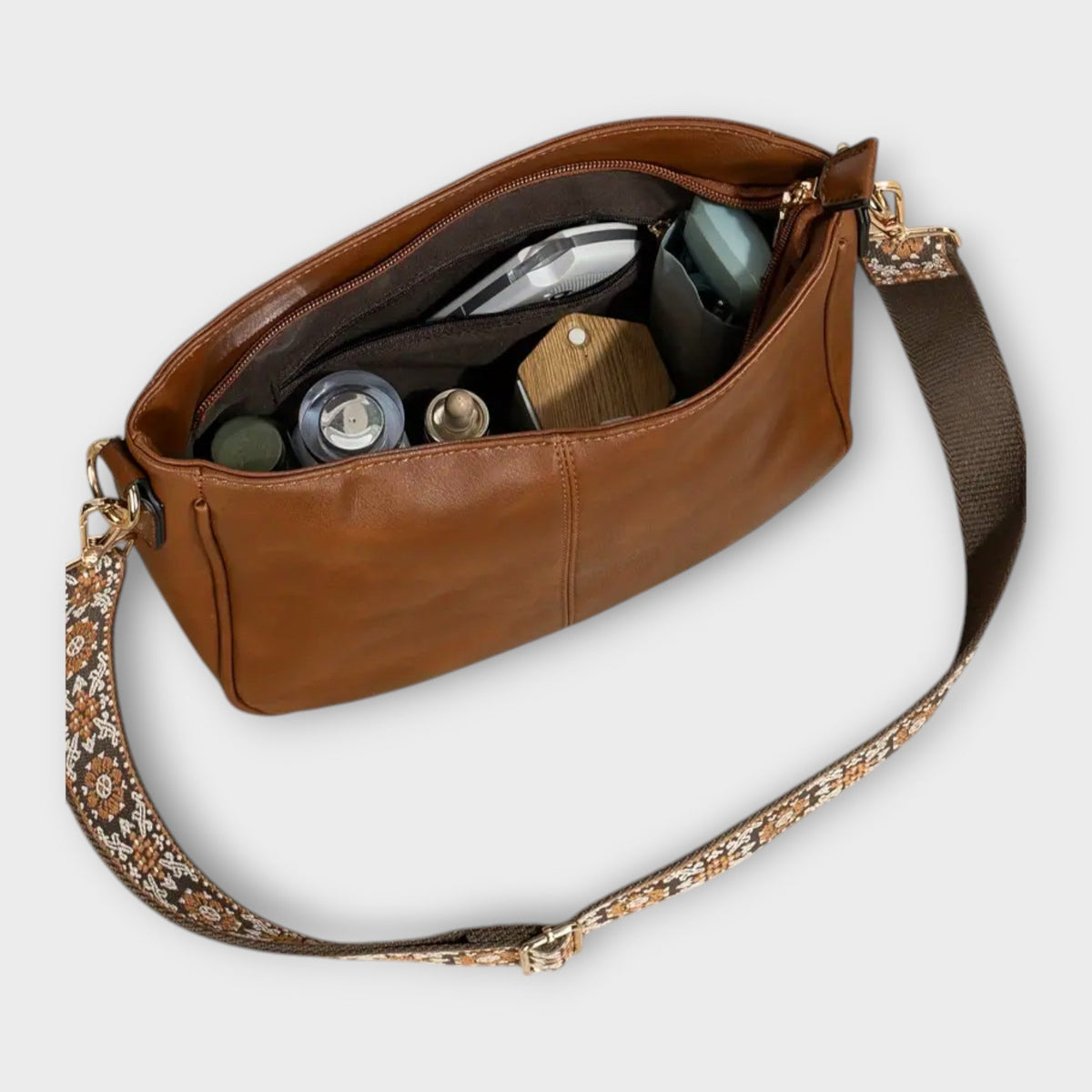 Brown crossbody bag open showing interior pockets and small bottles, patterned strap