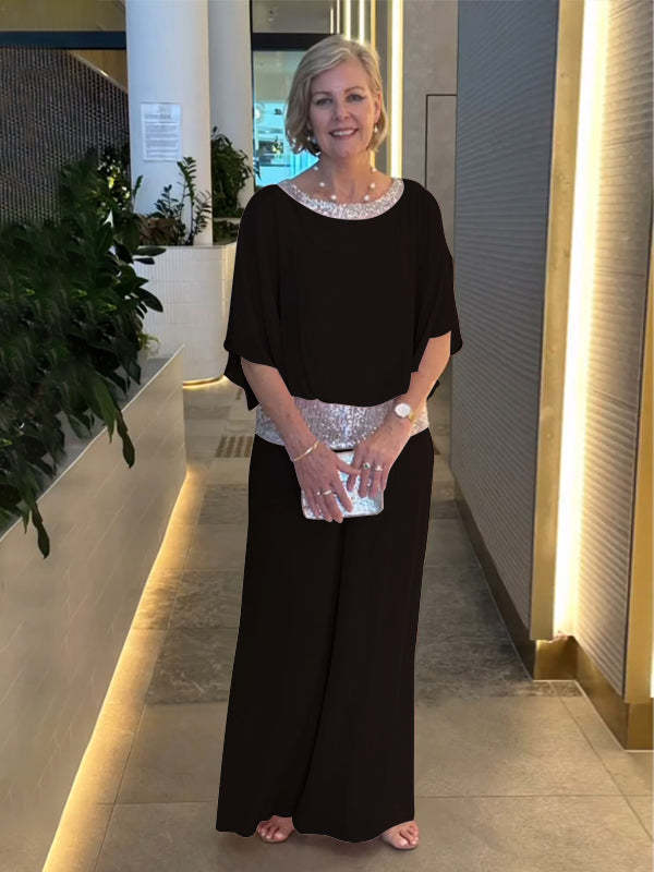 Ember elegant set in black: draped cape-sleeve top, wide-leg pants, rhinestone neckline, clutch.