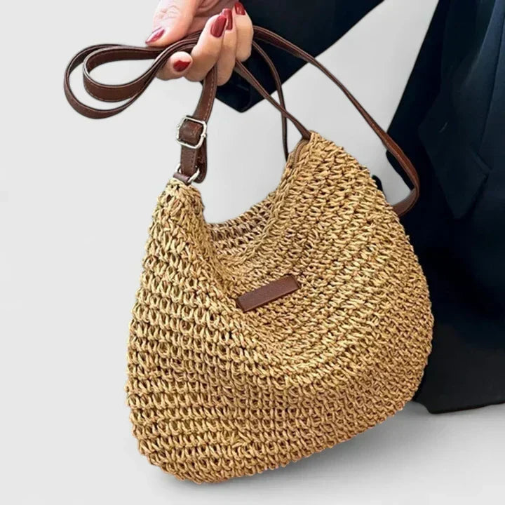 Handheld tan woven crescent bag with brown handles and rectangular logo patch