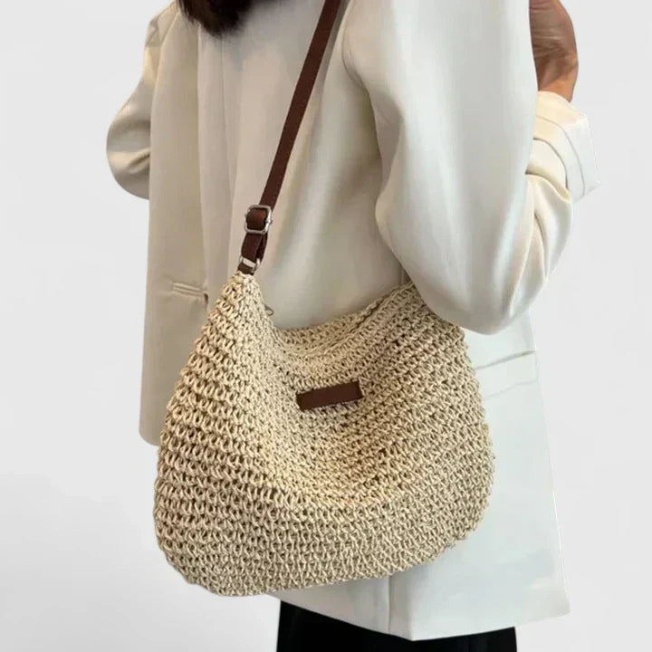 Beige woven crescent shoulder bag with brown strap and rectangular logo patch