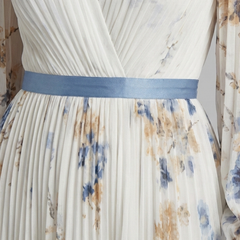 Cream pleated maxi dress close-up: V-neck bodice, blue waist sash, floral print
