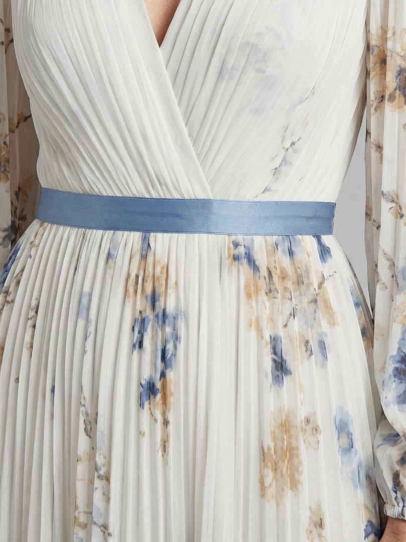 Cream pleated maxi dress close-up: V-neck bodice, blue waist sash, floral print