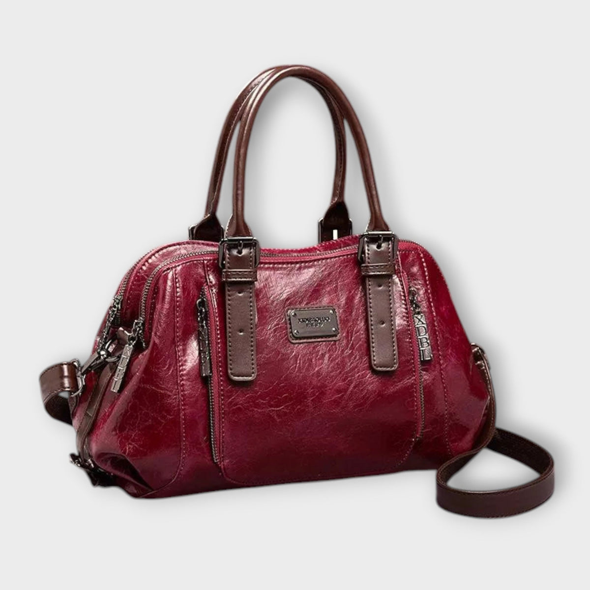 Red leather-look shoulder bag with top handles, front logo plaque, zip top, crossbody strap.