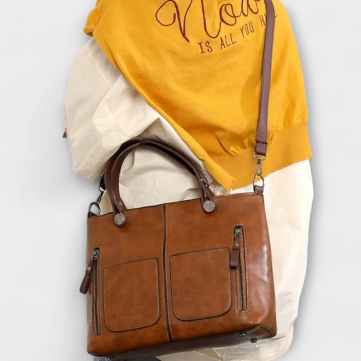 Brown leather tote bag with top handles, front pockets, and crossbody strap.