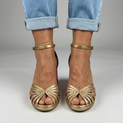 Gold heeled sandals with open toe, braided crossover straps, and ankle strap