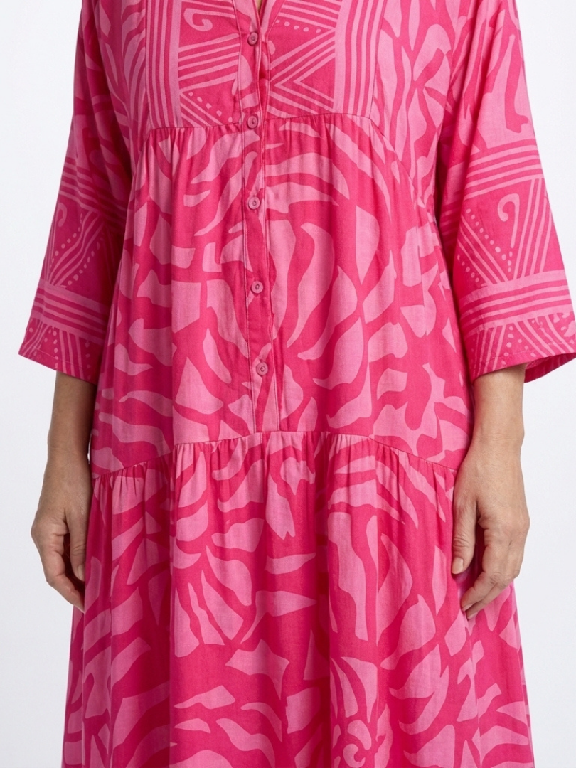Pink button-front midi dress close-up: V-neck placket and tiered skirt, patterned.